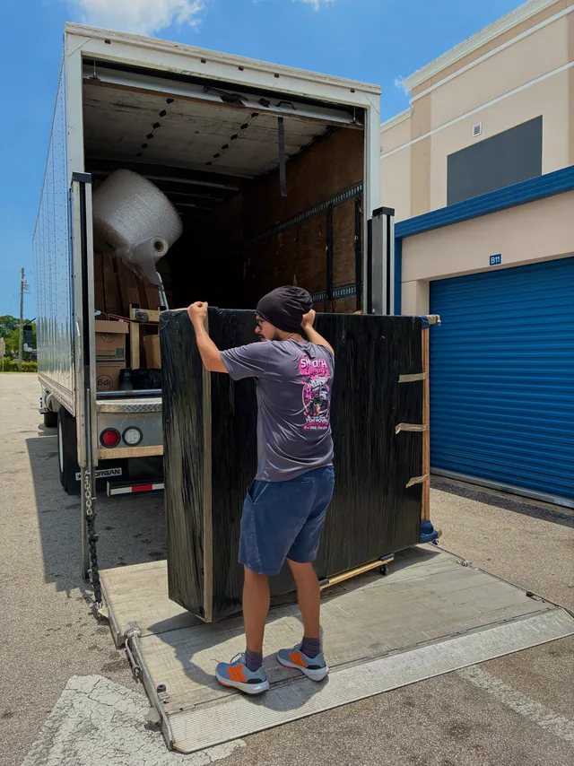 Two movers loading a large wrapped panel up the ramp